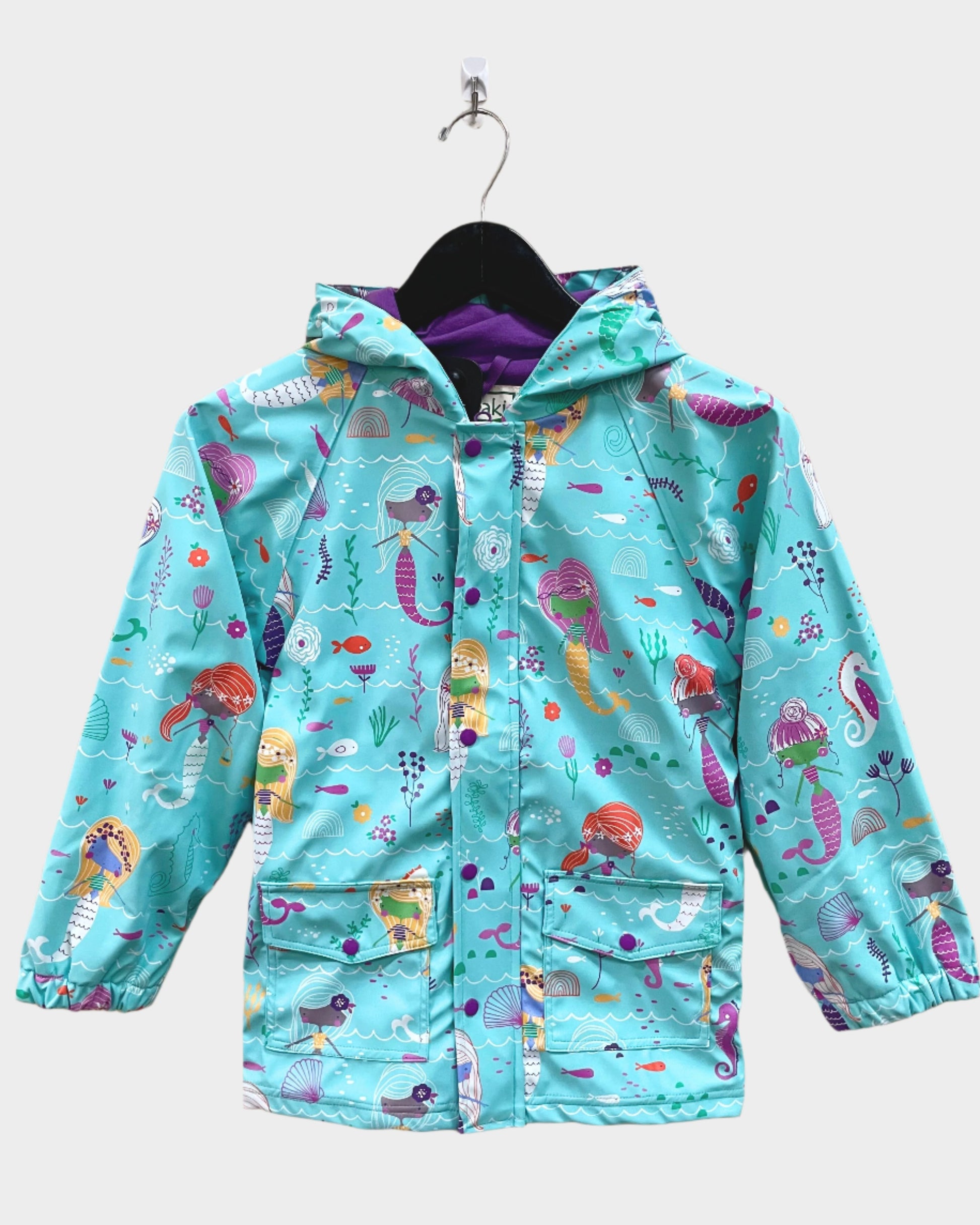 Kids lined rain coat with lining, attached hood, and pockets. Shown in mermaids pattern with a brought blue background, various mermaids, seahorses, and other underwater designs. 