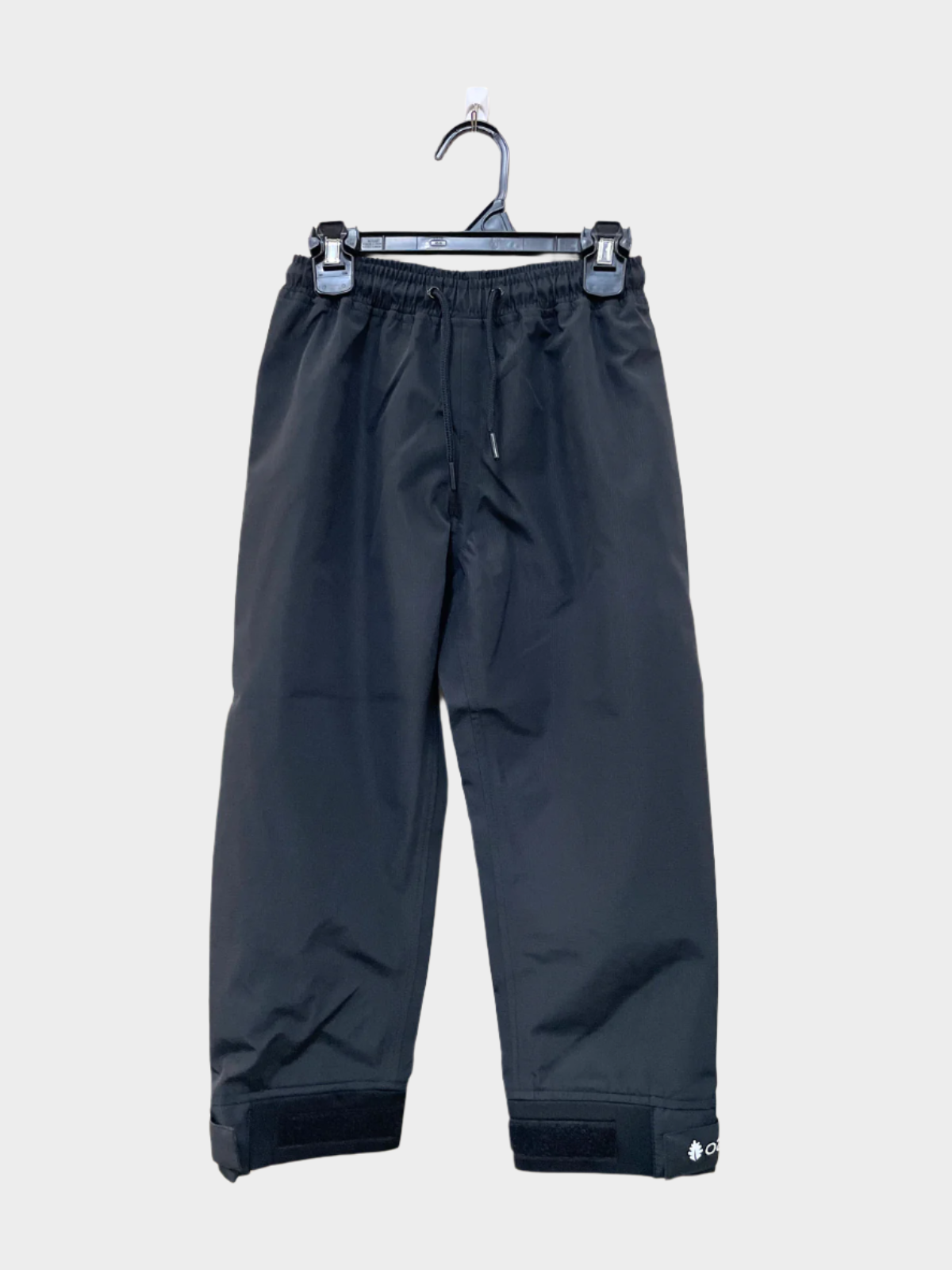 A pair of kids rain pants with an elastic waistband and drawstring. Ankles have a neoprene covered velcro adjustment. Shown in black