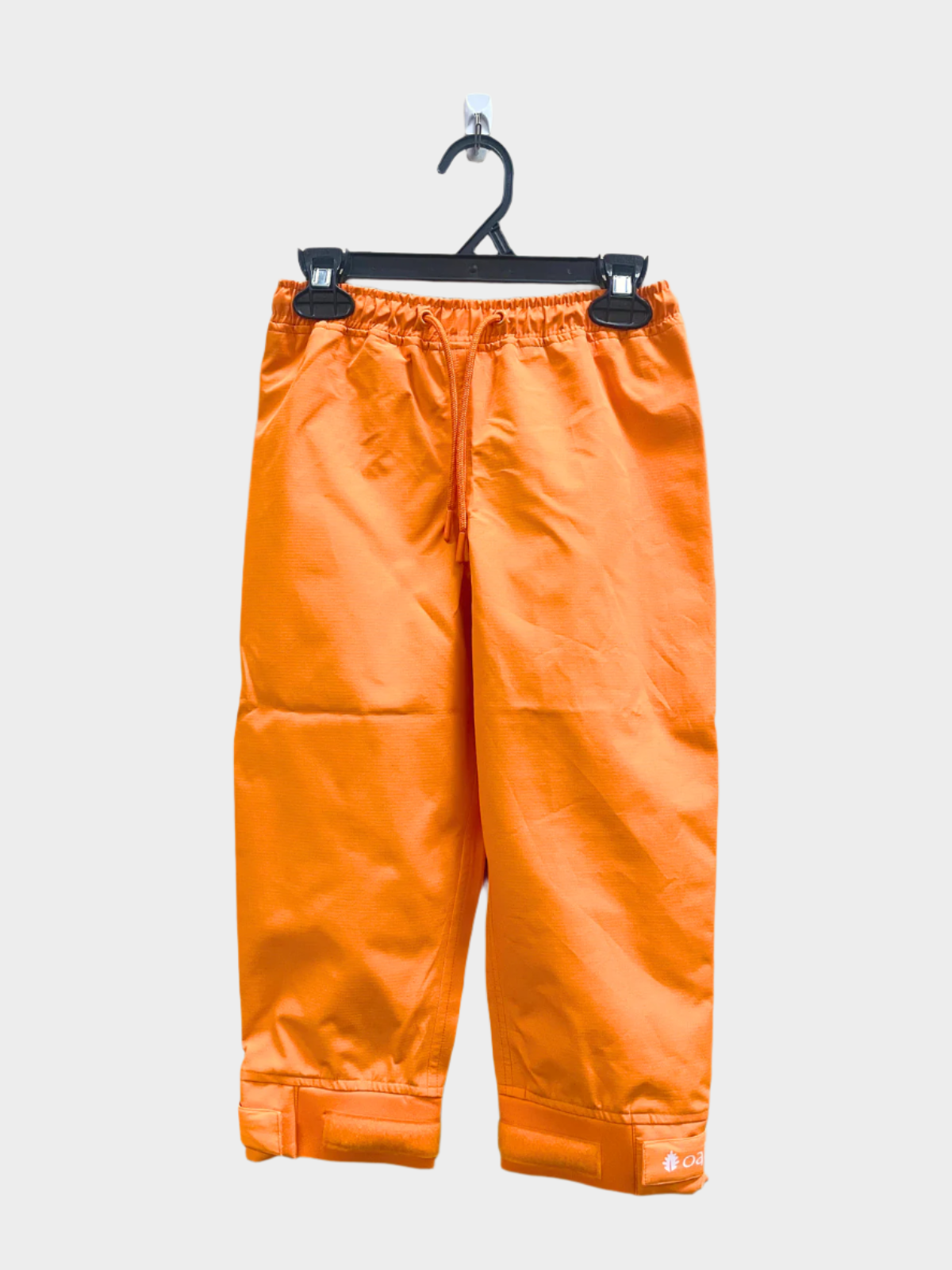 A pair of kids rain pants with an elastic waistband and drawstring. Ankles have a neoprene covered velcro adjustment. Shown in lava orange